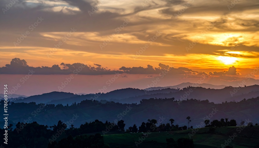 Naklejka premium Mountain ranges fade into distance beneath sunset, a painterly sky above
