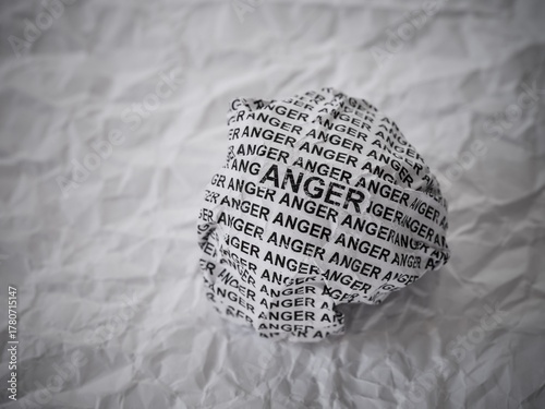 Crumpled paper ball with words Anger on a crumpled white paper background.