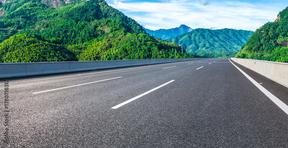 Fototapeta premium Empty asphalt highway road and majestic mountain natural landscape under a beautiful blue sky with clouds