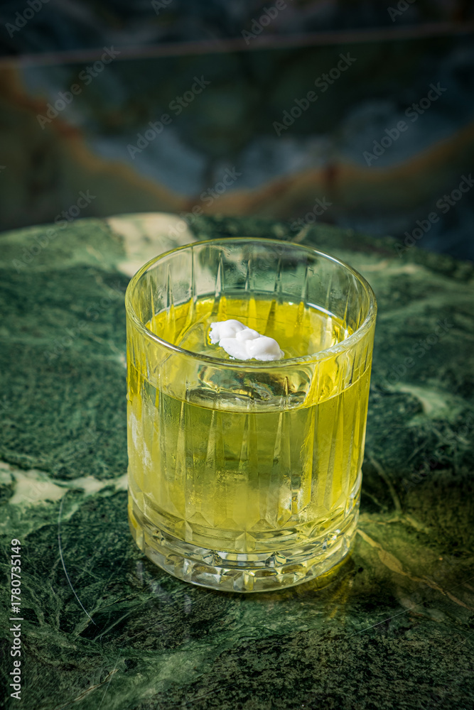 Obraz premium A vibrant green drink in a textured glass sits on a dark marble surface, inviting and cool