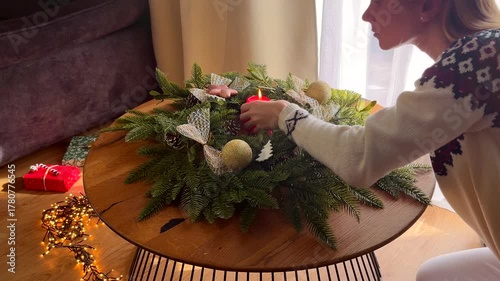 Woman in a Christmas sweater decorating a festive wreath with a candle, cozy home atmosphere