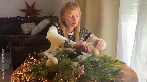 Woman in a Christmas sweater decorating a festive wreath, cozy winter holiday atmosphere at home