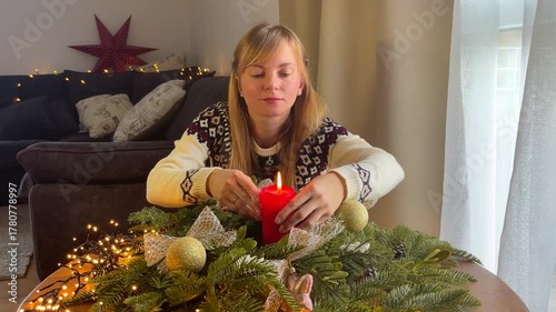 Woman in a Christmas sweater decorating a festive wreath with a red candle, cozy winter holiday mood at home