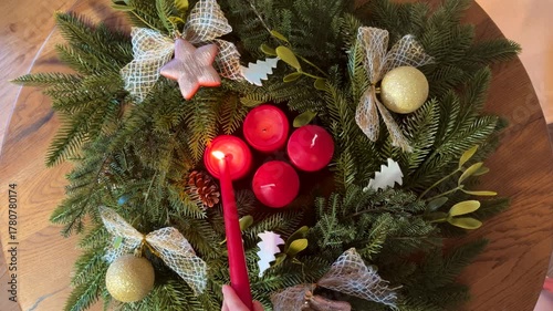 Top view of an Advent wreath with four red candles being lit by hand with candle, cozy Christmas atmosphere