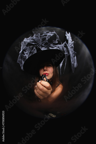 portrait of a young witch in hat on black background with spider net and holding chain  in her hands
