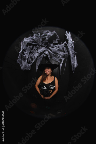 portrait of a young witch in hat on black background with spider net