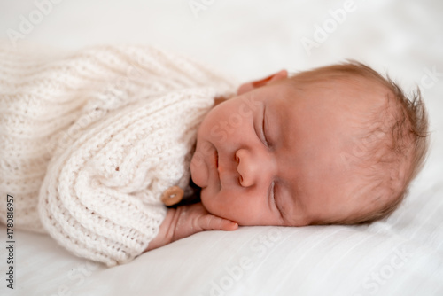 newborn baby sleeping on a white bed at home, close-up portrait of a newborn baby sleeping in a white knitted bodysuit, space for text