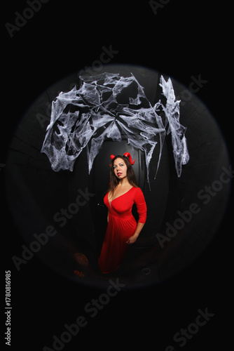 portrait of a young witch in red dress  with red horns on black background with spider net
