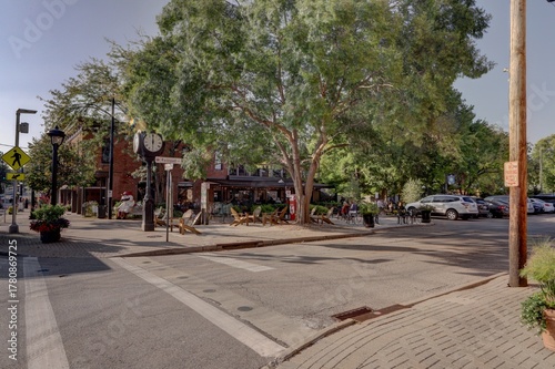 View of crosswalk lines cutting through asphalt streets leading to restaurants and shops shaded by green trees in Loveland, Ohio, United States, Loveland, Ohio, United States.