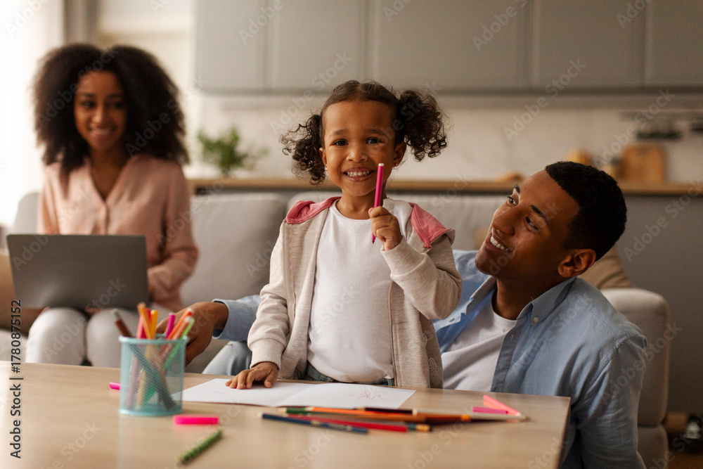 Fototapeta premium African American dad drawing with little daughter, spending quality time babysitting with child while mother working on laptop, sitting nearby