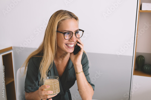 Fotomural Close-up of excited female freelancer on phone holding glass of juice, emphasizi