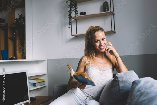 Cuadro en lienzo Smiling freelancer with book in hand, sitting comfortably on sofa, enjoying mome