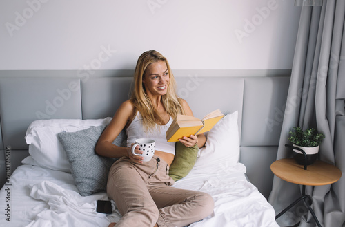 Fotografía Smiling woman enjoying book and coffee on bed, expressing comfort, warmth, and b