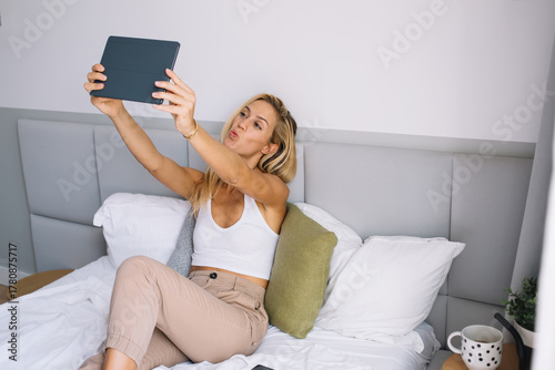 Cuadro en lienzo Young woman taking playful digital selfie with tablet while sitting in bed, repr