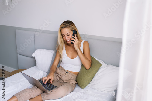 Cuadro en lienzo Young woman smiling while having phone call and typing on laptop from bed, refle