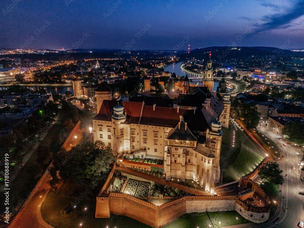 Obraz premium Aerial evening view of Wawel Castle in Kraków, Poland, with illuminated walls and Vistula River