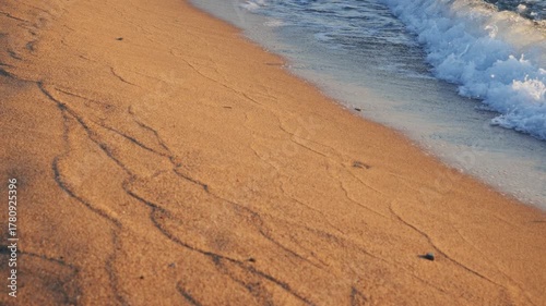 Sandy beach with gentle waves lapping at the shore. The sand has visible patterns and textures created by the water.