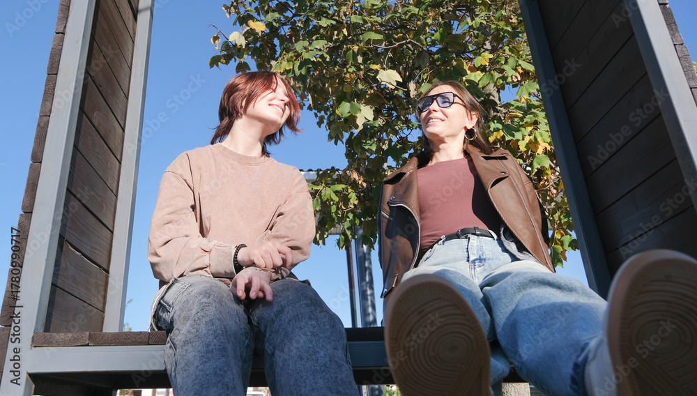 Fototapeta premium girl and mother sitting on urban park bench talking