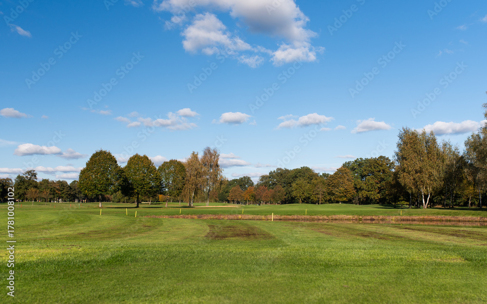 Fototapeta premium Golf course with pond and trees under clear blue sky