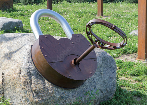 A large rusty metal padlock with a decorative key on a stone outside