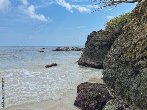 Tropical rocky beach with crystal-clear turquoise waters and blue skies - A secluded coastal landscape with cliffs and lush vegetation