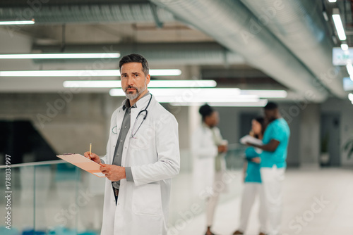 Male doctor holding clipboard and observing hospital hall