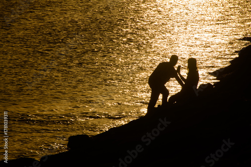 silhouette of a man and woman looking at a phone against a glistening sea.