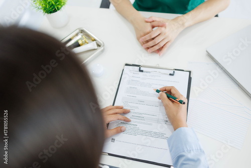 A woman is talking to a man in a medical setting. The woman is holding a pen and the man is holding his hand up. There are several bottles and a laptop on the table. Scene is serious and professional
