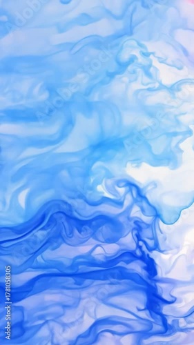 Blue ink spreads gracefully through water creating organic clouds and flowing textures that merge into a smooth abstract composition