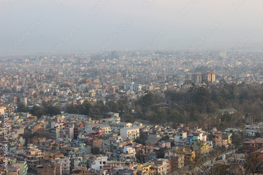 Obraz premium Wide panoramic view of a densely populated cityscape with clusters of buildings extending toward the horizon under a hazy sky.