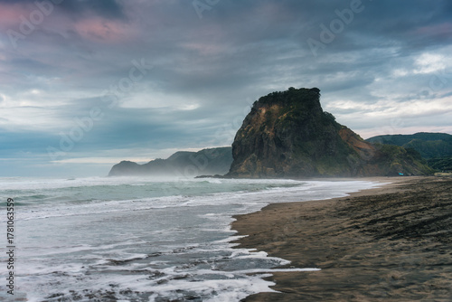 Lion Rock mountain on Piha Beach with breaking wave in the evening at New Zealand