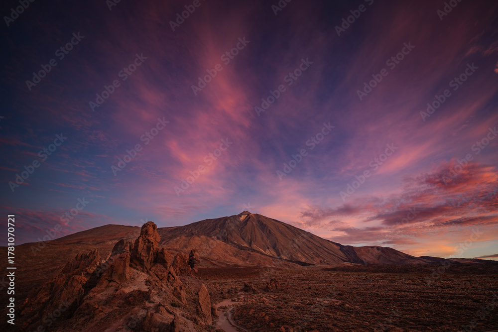 Naklejka premium Vibrant sunset sky over Mount Teide in Tenerife, Canary Islands. Dramatic colorful clouds illuminate the volcanic landscape during the golden hour. A stunning scene capturing the beauty of Teide