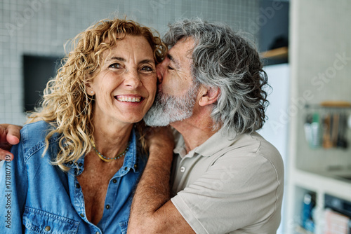 Portrait of happy senior mid aged mature couple prepering meal with fresh vegatebles in kitchen at hpme