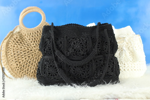 Crocheted bags in different colors and varieties arranged on a white fluffy blanket in front of a blue background.
