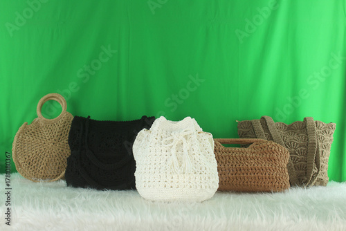 Crocheted bags in different colors and varieties arranged on a white fluffy blanket in front of a green background.