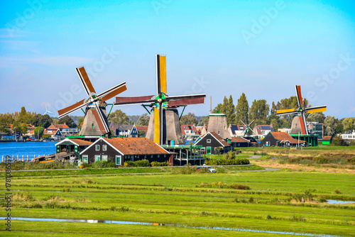 Scenic landscape of a European rural village with windmills, fields, and water under a bright, clear sky