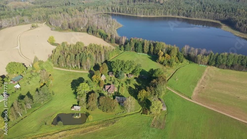 Aerial view of a serene rural landscape showcasing vibrant greenery, a tranquil pond, and a winding path, with a gradual zoom out revealing expansive surroundings