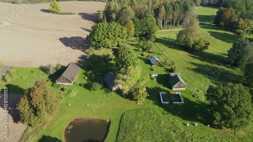Aerial view of serene rural landscape showcasing lush greenery, rustic buildings, and a tranquil pond, with camera smoothly zooming in on the scene's details