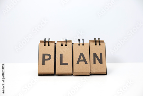 Table sign with the word PLAN placed on a white desk with white background. Minimal business concept representing strategy, planning, goal, and future vision