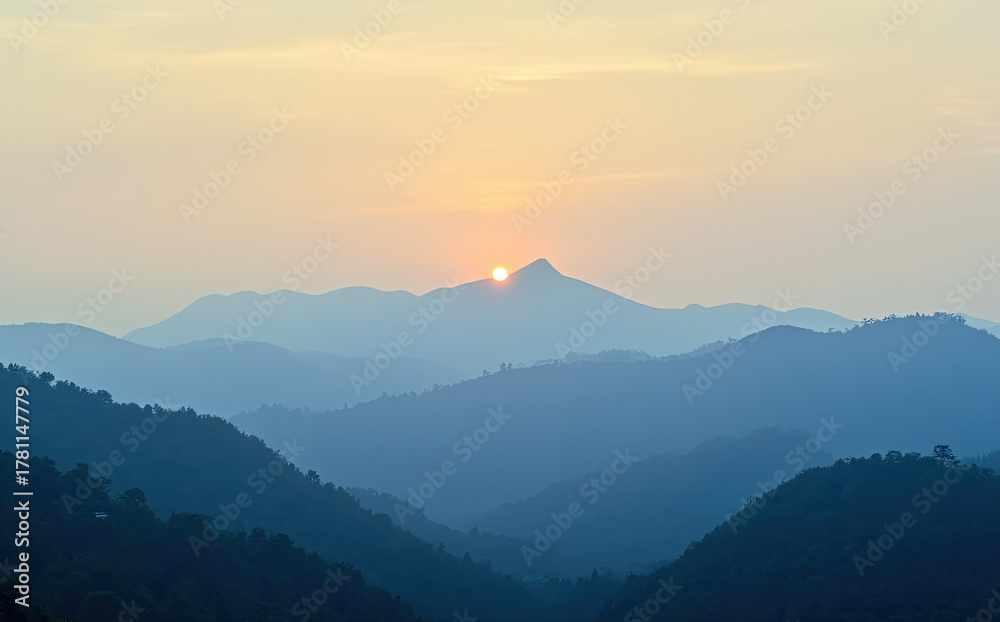 Obraz premium Golden sun crests hazy blue mountain range at dawn mountains sunrise