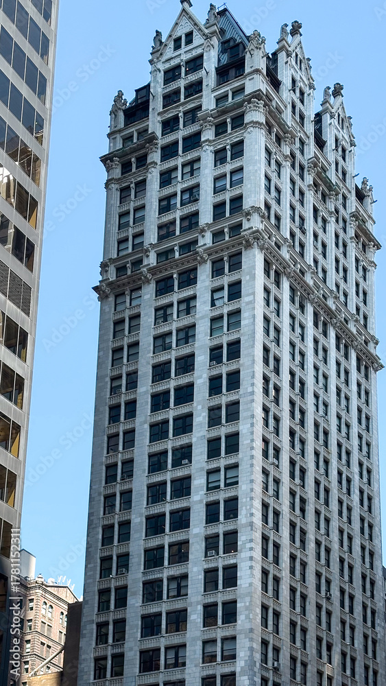 Obraz premium Historic skyscraper with ornate architecture amidst modern buildings in urban landscape concept of architecture firms, history publications, real estate agencies