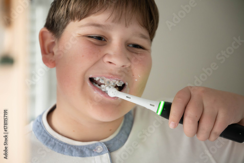 Smiling boy brushing teeth with an electric toothbrush and braces. Concept of oral hygiene, dental care, and orthodontic cleaning for kids.
