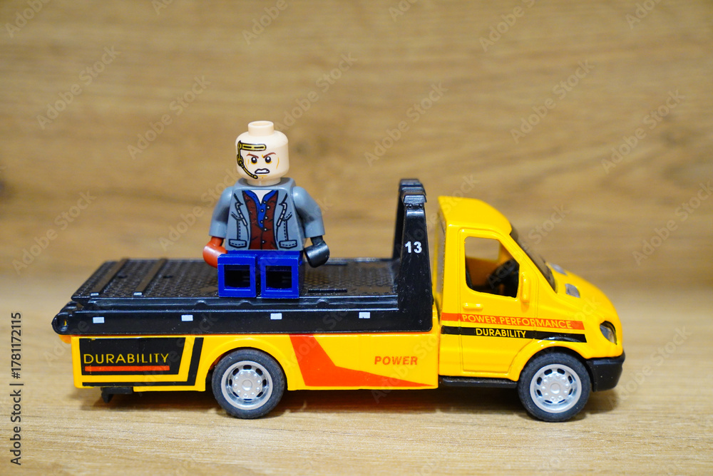 Obraz premium Lego minifigure on a yellow toy truck with a wooden background