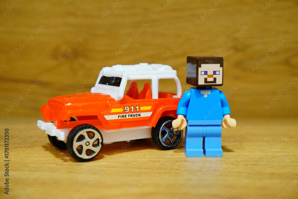 Naklejka premium A Minecraft Steve minifigure stands next to a toy fire truck on a wooden surface