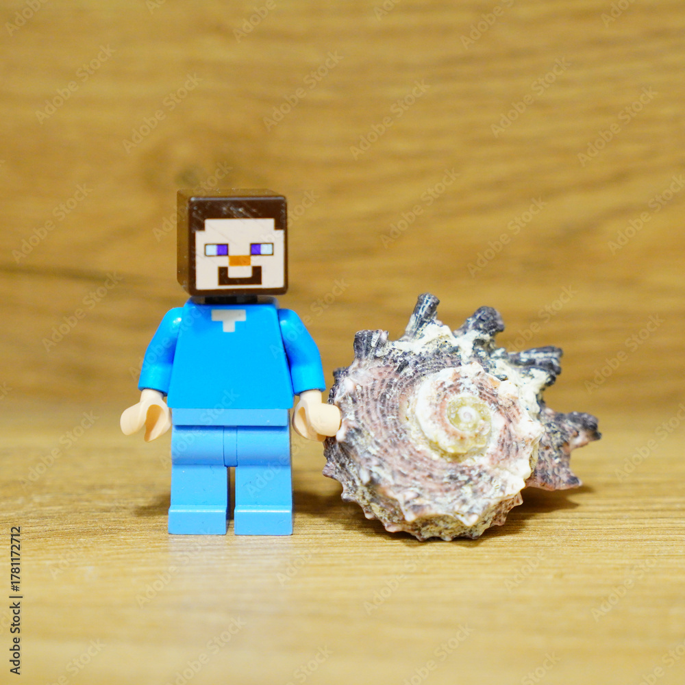 Fototapeta premium Minecraft Steve figure stands next to a beautiful seashell on a wooden surface