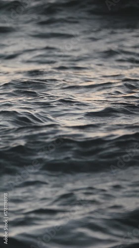 Waves gently move on the sea surface during sunrise with sunlight reflections creating shimmering bokeh and calm relaxing mood.