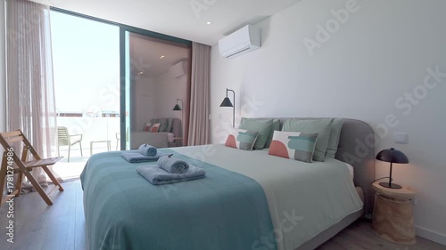 Natural light illuminates a modern hotel room featuring a comfortable bed, stylish decor, and access to a private balcony with ocean views, creating a relaxing and inviting atmosphere