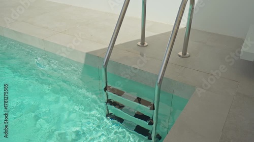 Crystal clear turquoise water gradually fills a contemporary swimming pool, inviting viewers to imagine a refreshing plunge into its cool depths on a sunny day