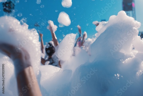 Hands reach up through a mountain of white foam, capturing the excitement of a lively foam party. The image radiates fun, energy, and carefree celebration.