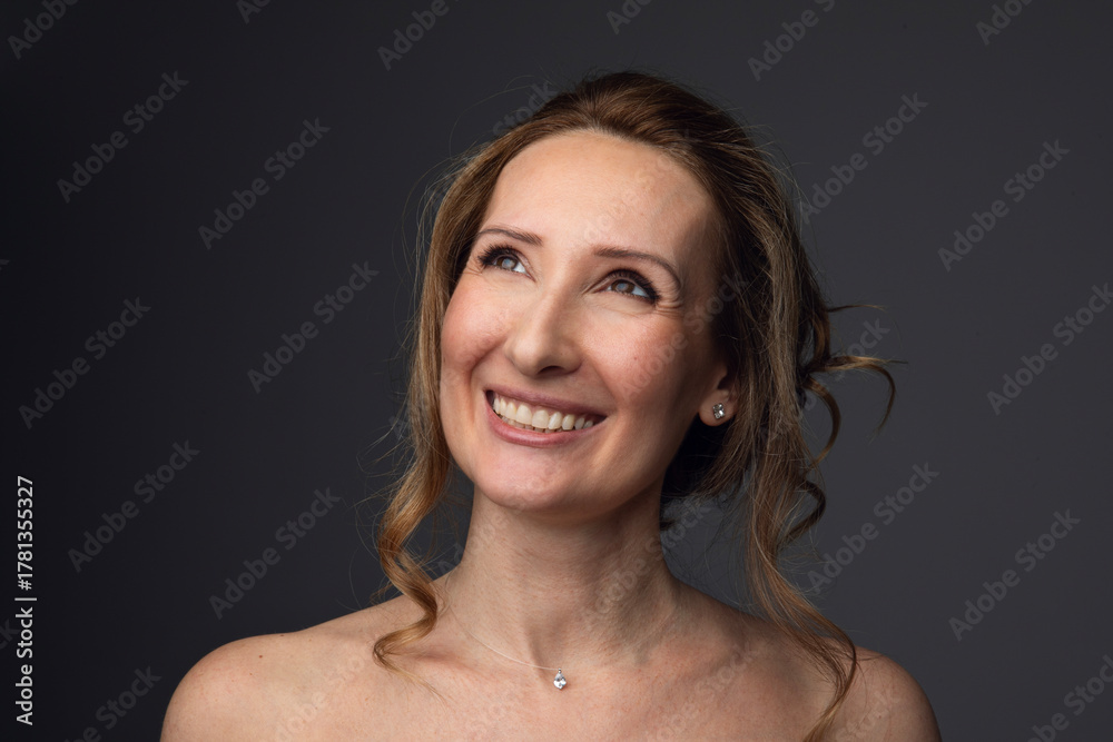 Obraz premium Closeup photo of a happy beautiful woman, looking at camera, holding a hands near neck, isolated grey background.